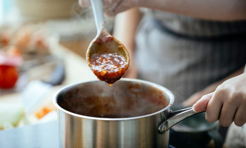 Panela pequena com calda de frutas vermelhas sendo mexida com colher de pau